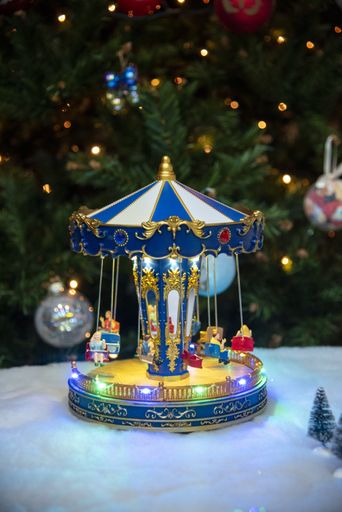 A vertical shot of a child carousel ornament with the decorated Christmas tree in the background