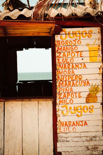 A vertical shot of an old wooden bar with a juice menu sign and a seascape view