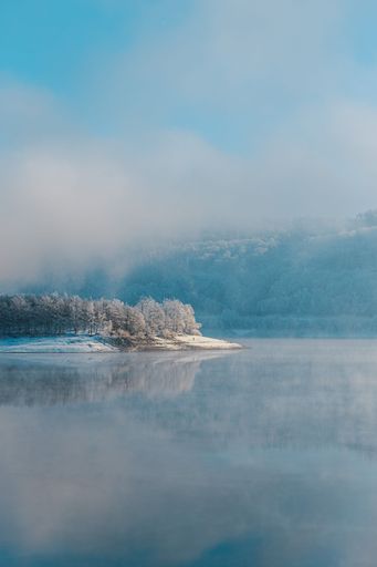 A pristine winter landscape with a frozen lake covered in a blanket of snow and fog