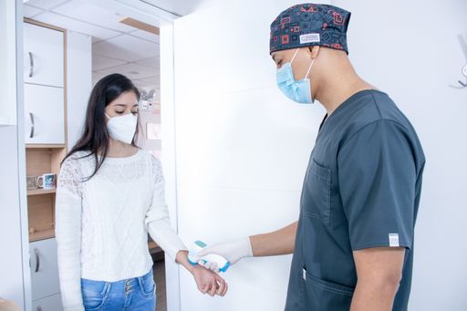 A doctor checking a female's temperature before entering the clinic