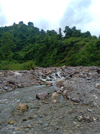 A vertical shot of a river flowing through rocks with green hills in background