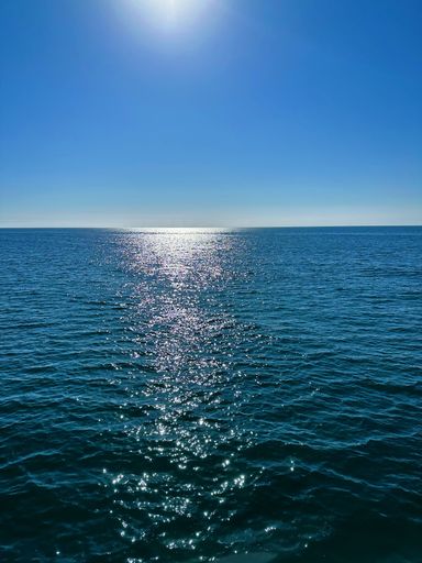 A vertical shot of a sea with sunlight under blue sky