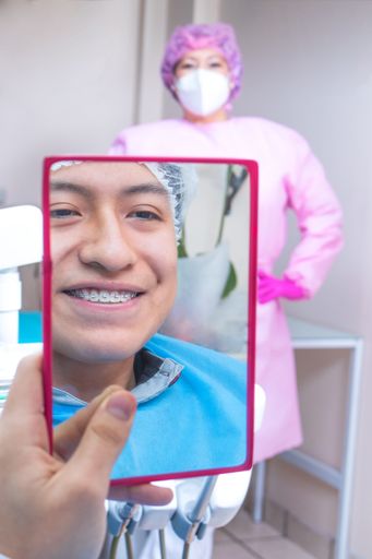 A happy patient in dentistry with teeth brackets looking in the mirror and smiling