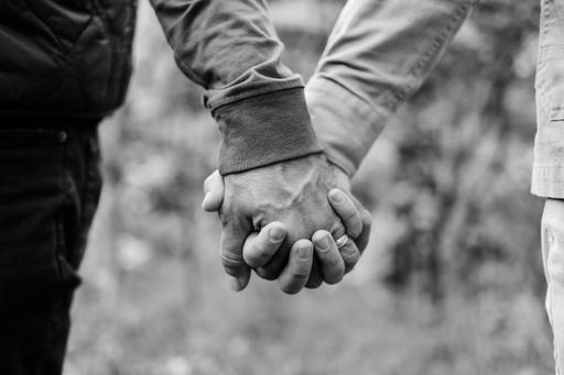 Two male silhouettes standing side by side and holding hands in a black and white image