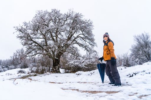 A woman in a yellow jacket walking on snowy path during winter in the town of Opakua near Vitoria in Araba, Basque Country, Spain