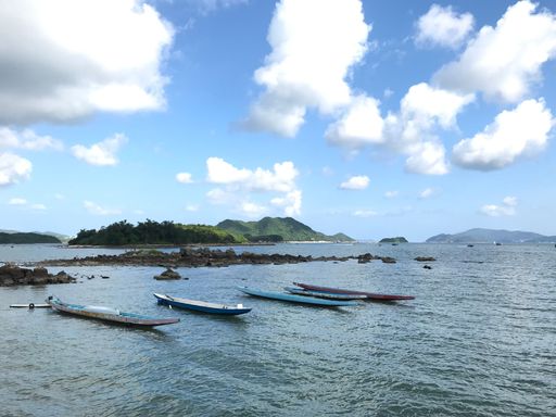A row of long rowing boats on peaceful waters surrounded by green hills under a bright cloudy sky