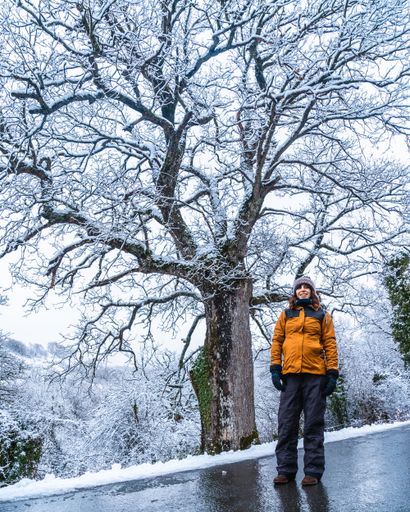 A vertical shot of a woman in a yellow jacket under a snowy tree during winter in the town of Opakua near Vitoria in Araba, Basque Country, Spain