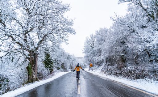 A woman in a yellow jacket walkinon an icy road lined with bare trees during winter in the town of Opakua  Basque Country, Spain