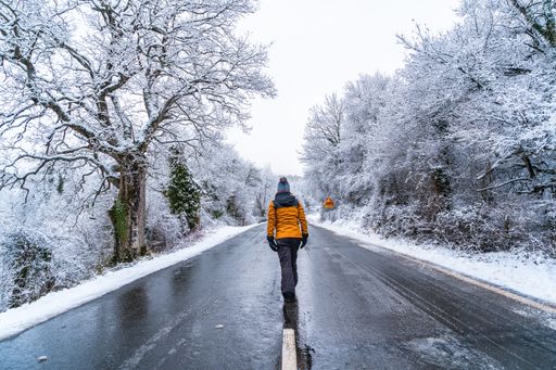 A woman in a yellow jacket walkinon an icy road lined with bare trees during winter in the town of Opakua in Basque Country, Spain
