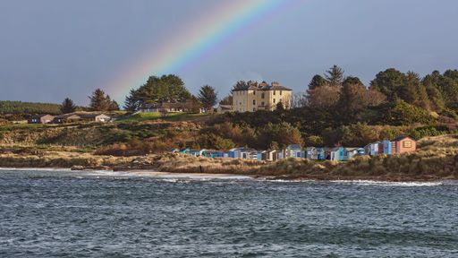A stunning view of a vibrant rainbow arching over a row of houses located near a tranquil coastline