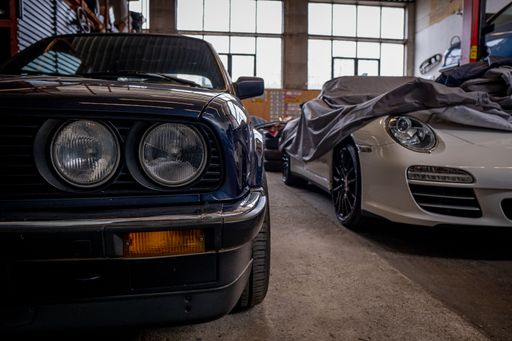 A blue BMW and a white 911 Porsche with a shower cap parked in a garage