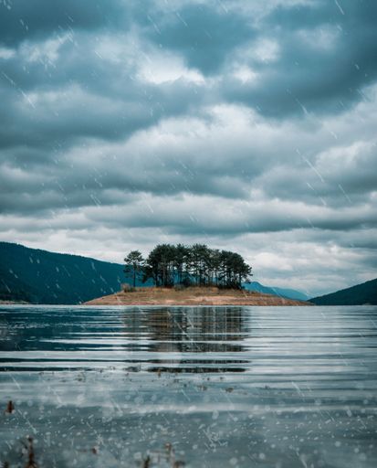 A vertical shot of a small island surrounded by a blue lake in cloudy sky background, Dospat, Bulgaria