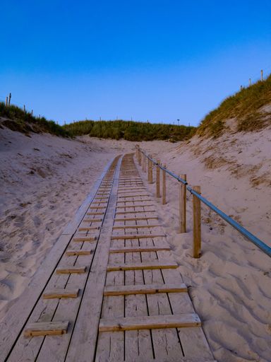 A vertical shot of the wooden stairs at the beach surrounded by small green hills at sunset