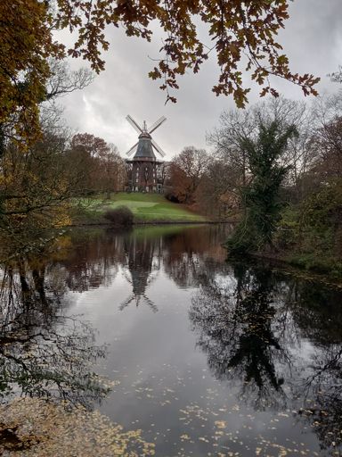 A river surrounded by autumn-colored trees with a background of a windmill