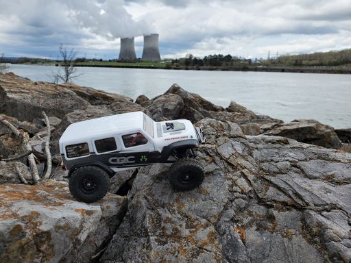 A toy car Jeep Wrangler on stones by the lake with a view of nuclear power plant
