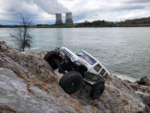 A toy car Jeep Wrangler on stones by the lake with a view of nuclear power plant