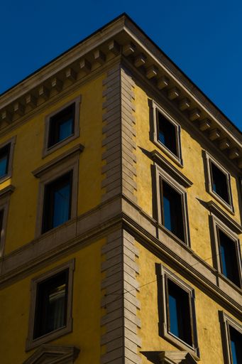 A vertical low angle shot of a bright yellow building against the bright blue sky, Rome, Italy