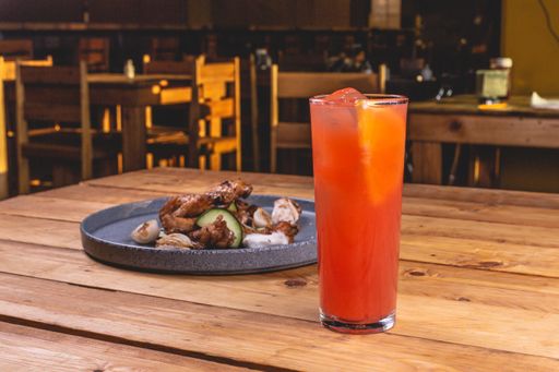 A closeup of delicious saucy chicken wings on a plate next to a refreshing drink on a wooden table