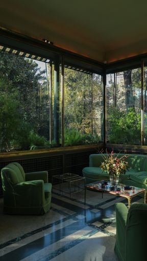 A vertical shot of the interior of a green living room with a forest view outside it