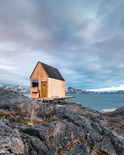 A vertical shot of a small wooden building in a rocky place near the lake under the gloomy sky