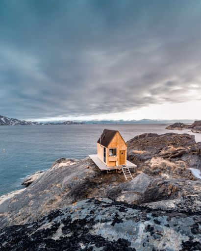 A vertical shot of a small wooden building in a rocky place near the lake under the gloomy sky