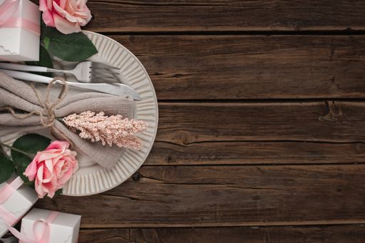 A closeup of a plate, rose, gifts, and table napkin with flowers on a wooden table