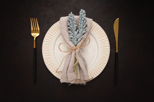 A closeup of knife, fork, and plate with a table napkin on top on a black background