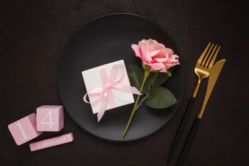 A closeup of knife, fork, "February 14" words in cubes, and plate with gifts and flowers on top