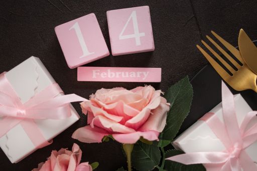 A closeup of "February 14" words in cubes, roses, gifts, plate, knife, and fork on a black background