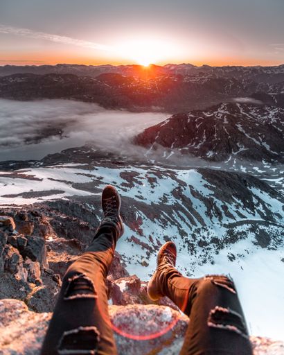A vertical shot of someone's feet in a mountainous foggy snow-covered area during the sunset