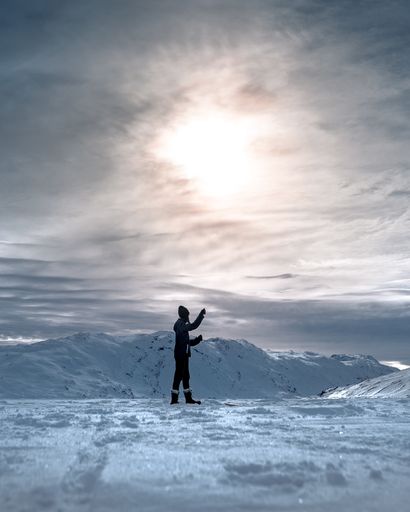 A vertical shot of a person fishing on a frozen lake under the cloudy sky