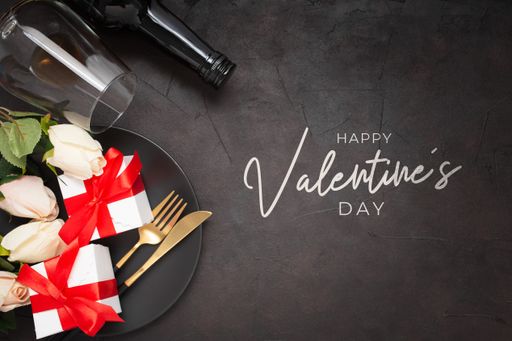 A closeup of a "Happy Valentine's Day" greetings with roses, knife, fork, wine glass, wine bottle, and gifts on a black background