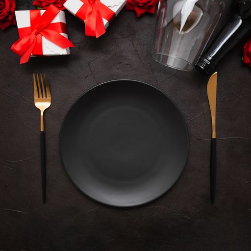 A closeup of a dinner plate, knife, fork, wine bottle, wine glass, gifts, and roses on a black background