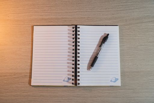 A high angle shot of an open blank notepad with a black pen on a wooden desk