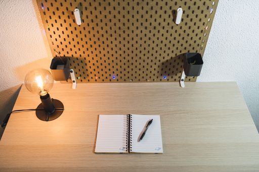 A high angle shot of an open blank notepad with a black pen and a lamp on a wooden desk