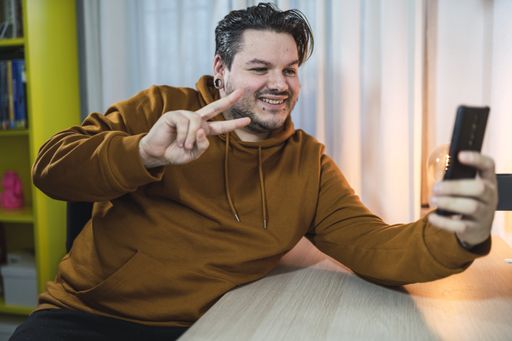 A selective focus shot of a cool cheerful guy with piercings taking a selfie showing the peace sign