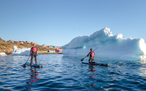 Two paddleboarders sailing with icebergs in the Arctic north in Sisimiut