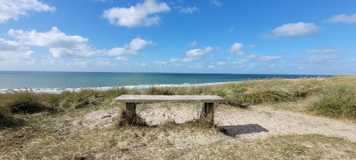 A panoramic shot of the sandy beach with a chair by the blue sea under a blue sky