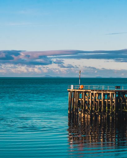 A vertical shot of the beautiful blue sea with a boardwalk and lighthouse at sunset