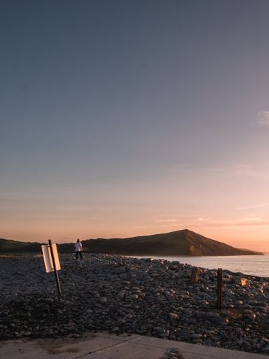 A vertical shot of the beautiful nature scene of the rocky beach and a person standing and watching the sea at sunset