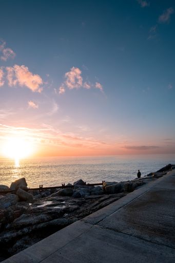 A vertical shot of the beautiful nature scene of the rocky beach and a person standing and watching the sea at sunset