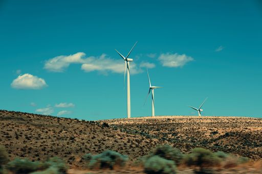 A scenic view of a rural area with three windmills on a field in blue sky background