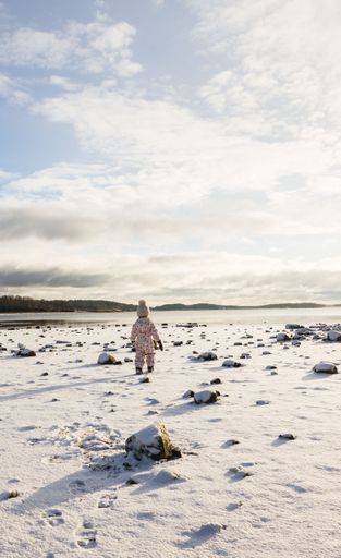 A scenic vertical shot of an adorable child walking in a snowy field during a beautiful winter day