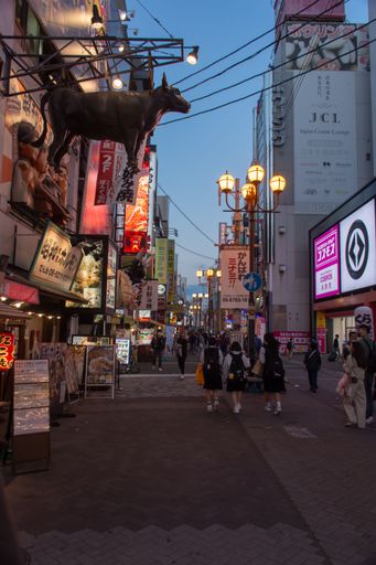 The nightlife of a crowded street in Osaka with neon lights, a pork statue at the top of the road, street foods, and restaurants