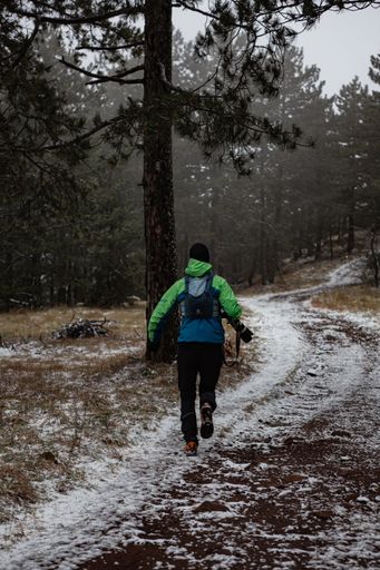 A vertical shot of a hiker running along a snowy path in the forest.