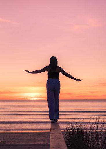 A female trying to keep balance while walking on a dock at the beach on the sunset