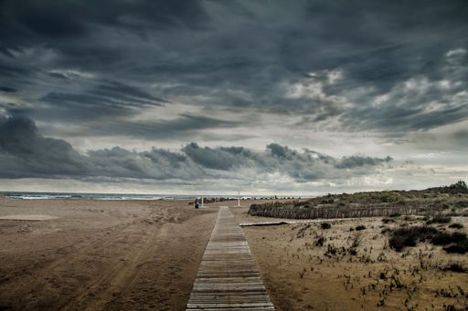 A horizontal view of a pathway leading to a beach through the sand under rain clouds