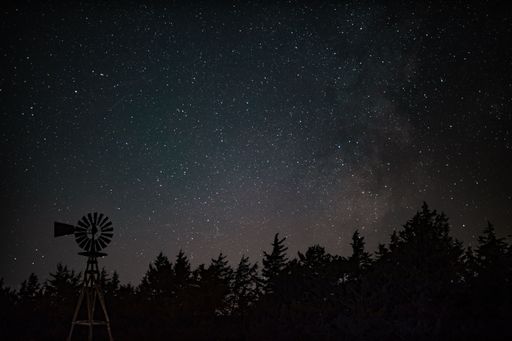 An astrophotography of the night sky taken over a single windmill in the rolling sandhills of Nebraska