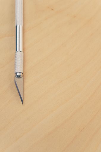 A vertical shot of the metallic scalpel on a plywood surface