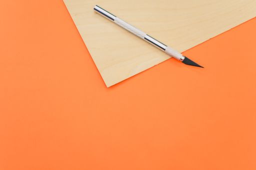 A high angle shot of the metallic scalpel on a plywood surface isolated on orange background